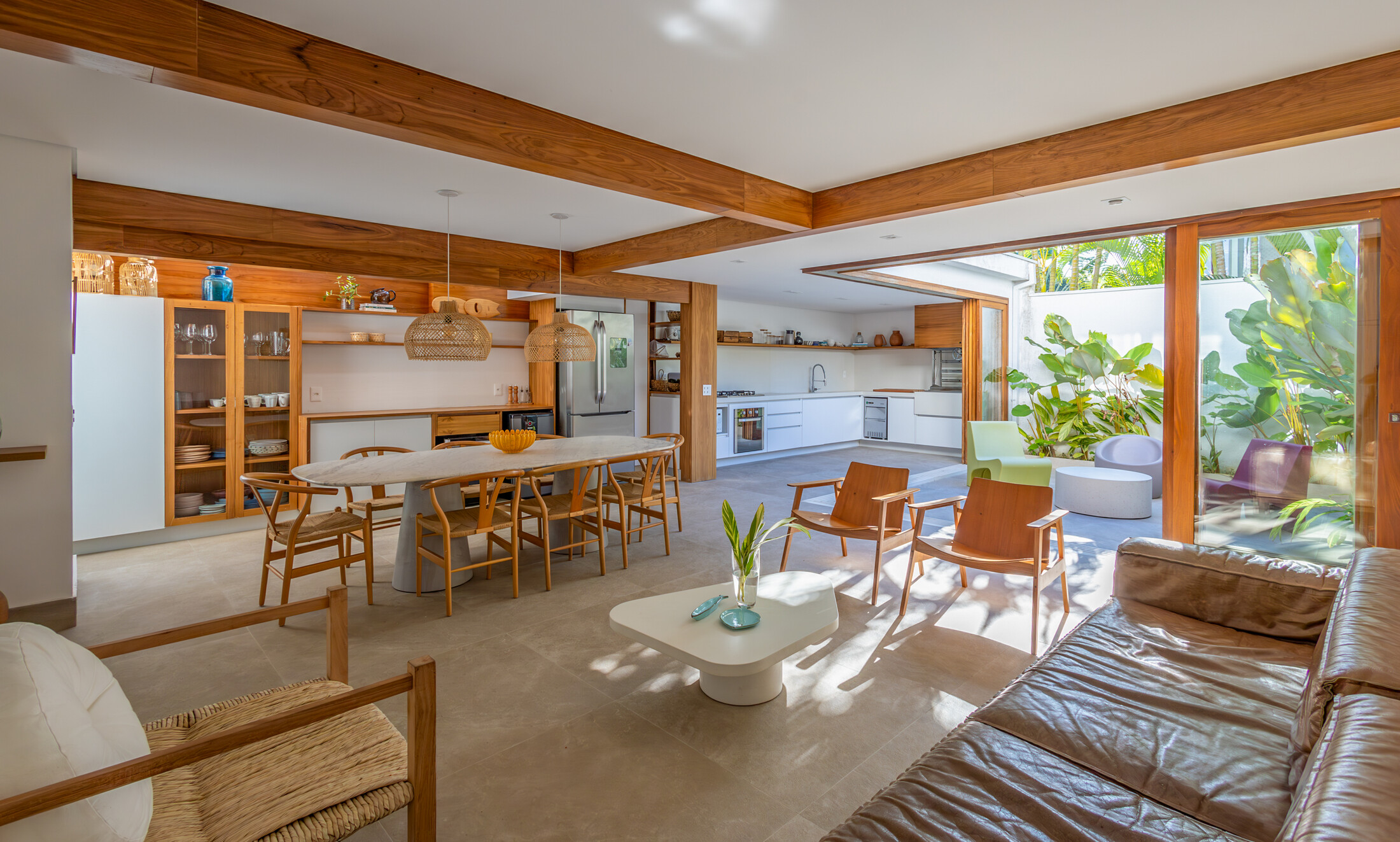 Sala de estar, jantar e cozinha integradas em madeira, abertas para um jardim tropical iluminado